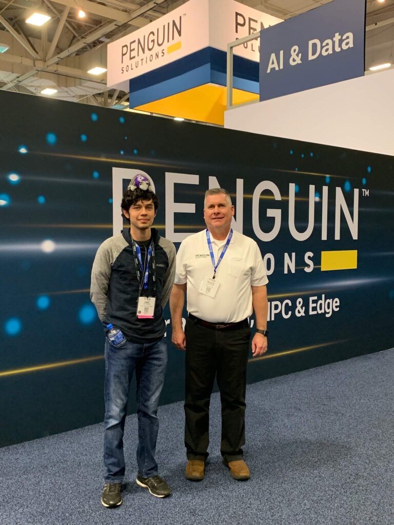 Two people standing in front of a large Penguin Solutions sign at a convention.